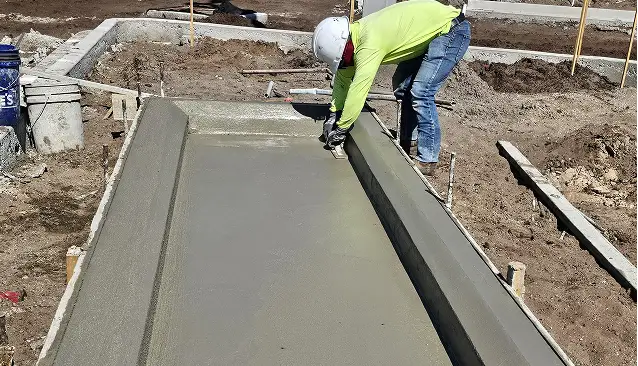 Construction worker smoothing concrete flumes edges of freshly poured concrete ramp for sidewalk accessibility
