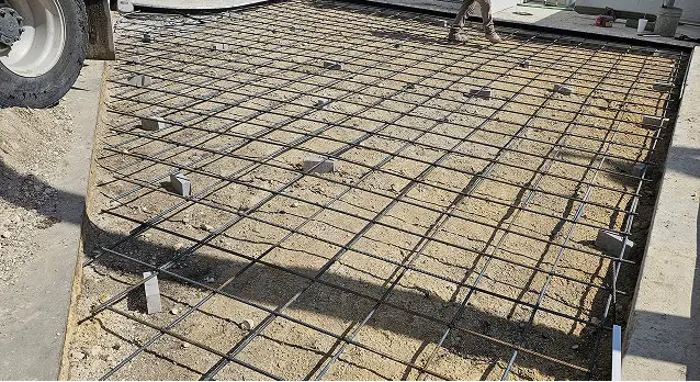 Parking lot steel rebar grid installed for concrete slab foundation at construction site.