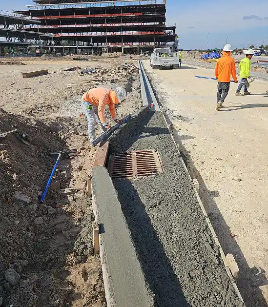 Construction worker shaping fresh concrete around a storm drain at a commercial site