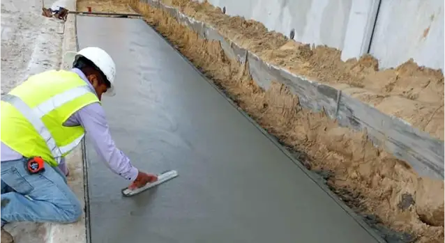 Construction worker using hand float to finish freshly poured concrete sidewalk.